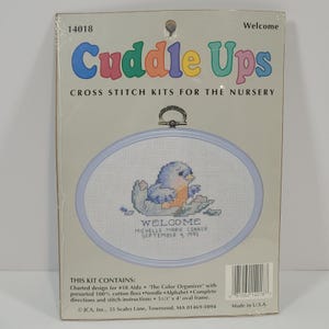 May include: A cross-stitch kit for the nursery, featuring a blue bird design inside an oval frame. The kit includes the text "Welcome" and the name "Michelle Marie Conner, September 4, 1995." The frame measures 5.5 inches by 4 inches.