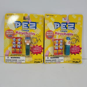 May include: Two PEZ candy keychain blister packs on yellow cardboard backing. One features an Uncle Sam character, the other a clown. Each includes two small PEZ candy packs. The packaging displays the PEZ logo, text, and safety warnings.