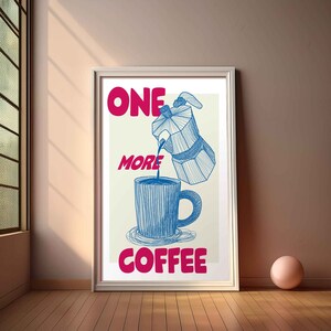 May include: A white framed poster with the text "ONE MORE COFFEE" in pink lettering. A blue illustration of a coffee pot pouring coffee into a blue mug is in the center of the poster.
