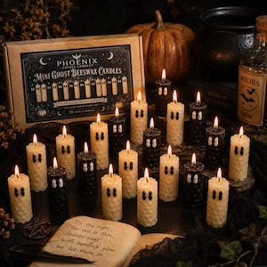 May include: A set of twenty mini ghost-shaped beeswax candles in black and cream colors, each featuring two small dots for eyes. The candles are displayed alongside a cardboard box labeled PHOENIX CANDLE COMPANY MINI GHOST BEESWAX CANDLES.
