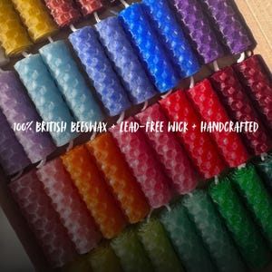 May include: A collection of colorful, handcrafted beeswax candles in various shades, including red, blue, and green. The candles have a honeycomb pattern and the text "100% BRITISH BEESWAX + LEAD-FREE WICK + HANDCRAFTED".