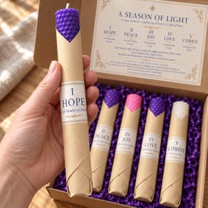 May include: A set of five honeycomb-textured taper candles in a cardboard box. Each candle is wrapped in brown paper with a label reading I Hope, II Peace, III Joy, IV Love, or V Christ. The box includes a printed guide titled A Season of Light.