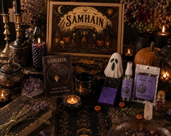 May include: A Samhain event box set featuring a large illustrated box, a book titled Samhain, a ghost-shaped item, a spray bottle, a tea pouch, a black mug, purple soap, candles, crystals, and dried flowers arranged on a dark surface.