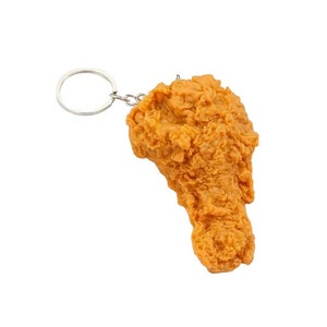 A fried chicken leg keychain with a silver metal ring. The chicken leg is a realistic replica of a fried chicken leg.