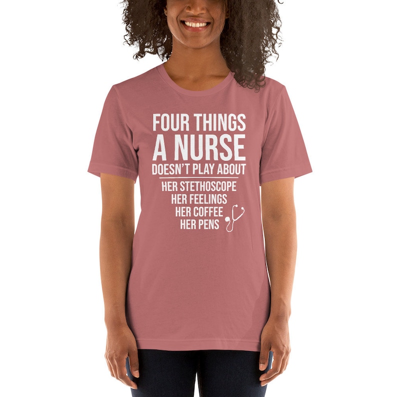 May include: A pink t-shirt with white text that reads "Four things a nurse doesn't play about: her stethoscope, her feelings, her coffee, her pens". A white stethoscope icon is next to the text.