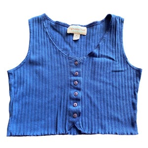 May include: A sleeveless, ribbed knit top in a vibrant blue hue. The top features a button-up front with six round, lavender-coloured buttons. The tag reads "Reference Point". The fabric has vertical ribbing, and the neckline is a subtle V-shape.