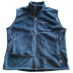 May include: A dark teal fleece vest with a full-length zipper and a stand-up collar. The vest has two zippered pockets and the brand name "patagonia" is embroidered on the chest. A small "R" logo is on the lower right.