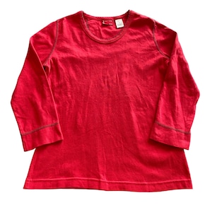 May include: A bright red long-sleeved shirt with a crew neck. The shirt has dark brown stitching along the seams and a small tag near the neckline. The sleeves are three-quarter length.