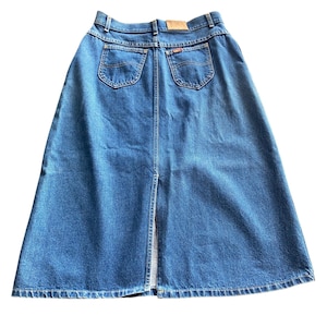 May include: A blue denim skirt with a high waist and a back slit. The skirt has two back pockets and a small leather patch on the waistband. The Lee logo is visible on the back pocket. The skirt is made of a medium-wash denim.