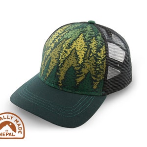 May include: A green and black trucker hat with a forest print on the front panel. The hat features a dark green brim and a mesh back. The hat has a small patch that says "Ethically Made in Nepal".
