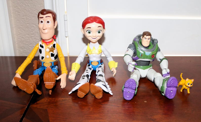 Puede incluir: Tres figuras de personajes de Toy Story: Woody, Jessie y Buzz Lightyear, junto con una peque&ntilde;a figura de gato amarillo. Woody viste un atuendo de vaquero, Jessie tiene un look de vaquera y Buzz lleva un traje espacial.