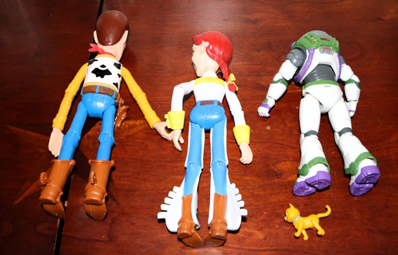 Puede incluir: Tres figuras de personajes de Toy Story: Woody, Jessie y Buzz Lightyear, junto con una peque&ntilde;a figura de gato amarillo. Woody viste un atuendo de vaquero, Jessie tiene un look de vaquera y Buzz lleva un traje espacial.