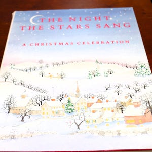 May include: A book cover with the title "THE NIGHT THE STARS SANG" and the subtitle "A CHRISTMAS CELEBRATION." The cover art depicts a snowy village scene with houses, trees, and a church under a starry sky, evoking a festive holiday theme.