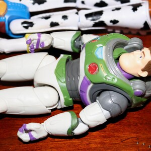 Puede incluir: Primer plano de dos figuras de acci&oacute;n de Toy Story. Buzz Lightyear lleva un traje espacial verde, blanco y morado. Jessie tiene un dise&ntilde;o de vaca en blanco y negro. Las figuras est&aacute;n sobre una superficie de madera, mostrando sus dise&ntilde;os detallados.