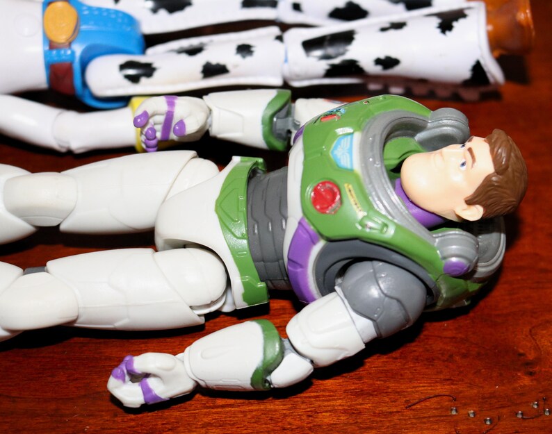 Puede incluir: Primer plano de dos figuras de acci&oacute;n de Toy Story. Buzz Lightyear lleva un traje espacial verde, blanco y morado. Jessie tiene un dise&ntilde;o de vaca en blanco y negro. Las figuras est&aacute;n sobre una superficie de madera, mostrando sus dise&ntilde;os detallados.
