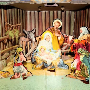 May include: A three-dimensional paper nativity scene featuring a stable structure with Mary, Joseph, and the infant Jesus in the center. Figures of shepherds, a donkey, a cow, and the three wise men are arranged around the central holy family.