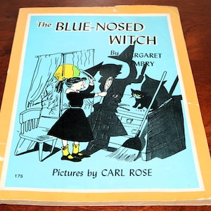 May include: A paperback book titled The Blue-Nosed Witch by Margaret Embry with pictures by Carl Rose. The light blue cover features a black and white illustration of a person in a dark dress, a black cat, a broom, and a witch's shadow.
