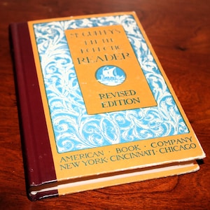 May include: A vintage orange and blue book titled "St. Cuffey's Eclectic Reader, Revised Edition" with a decorative floral design on the cover. The book is published by the American Book Company, New York, Cincinnati, Chicago.