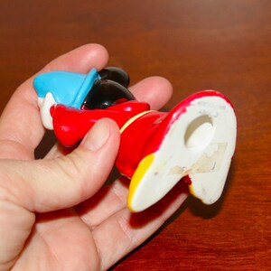 May include: A ceramic figurine of Mickey Mouse dressed as a sorcerer. He is wearing a blue hat, red robe, and yellow shoes. The figurine is about 6 inches tall and has a hole in the bottom for display.
