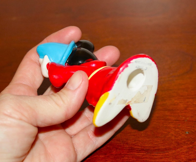 May include: A ceramic figurine of Mickey Mouse dressed as a sorcerer. He is wearing a blue hat, red robe, and yellow shoes. The figurine is about 6 inches tall and has a hole in the bottom for display.