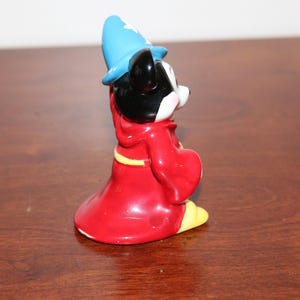 May include: A ceramic figurine of Mickey Mouse dressed as a wizard. He is wearing a red robe with a yellow sash and a blue pointed hat.