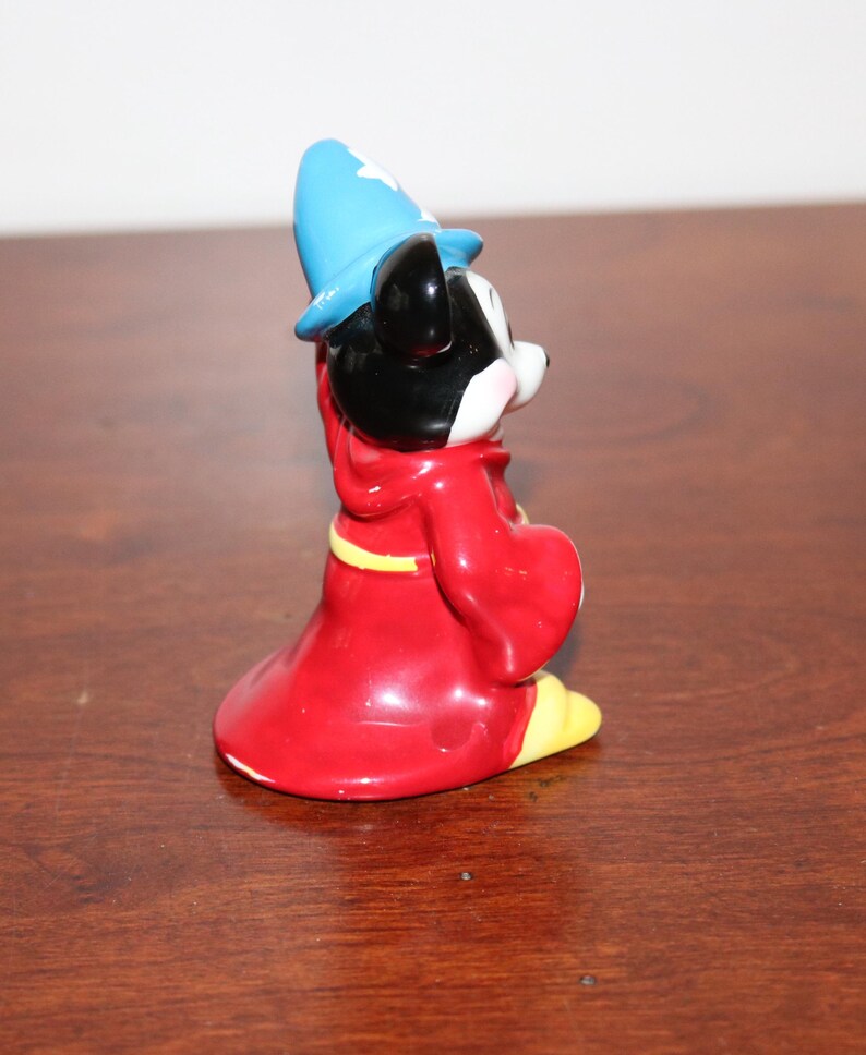May include: A ceramic figurine of Mickey Mouse dressed as a wizard. He is wearing a red robe with a yellow sash and a blue pointed hat.
