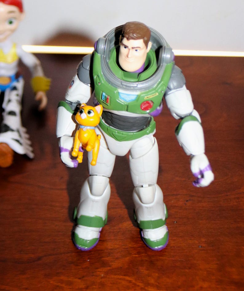 Puede incluir: Figura de acci&oacute;n de Buzz Lightyear con un traje espacial verde y blanco, sosteniendo una peque&ntilde;a figura de gato amarillo. La figura tiene una cabeza marr&oacute;n y un casco verde. El gato tiene un collar azul.