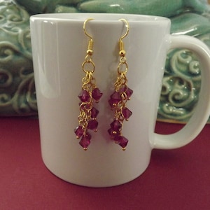 May include: Gold dangle earrings with a cascade of deep purple faceted glass beads.