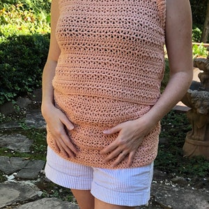 May include: A peach-colored crochet top with a high neck and sleeveless design. The top is made with a delicate open stitch pattern.