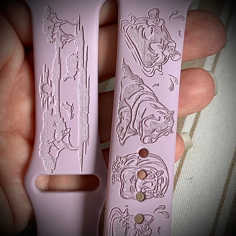 May include: A pink silicone watch band with a white engraved design of hippos and trees. The band has a cutout for the watch face.