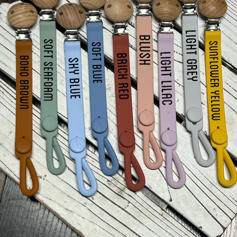 Pu&ograve; includere: Dieci clip per ciucci in silicone di vari colori, tra cui giallo girasole, grigio chiaro, lilla chiaro, blush, rosso mattone, blu chiaro, blu cielo, morbida schiuma di mare e marrone boho. Ogni clip ha una perla di legno e un fermaglio metallico.
