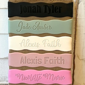 May include: Five personalized name tags with wavy edges. The tags are in black, green, white, pink, and light pink. The names on the tags are Jonah Tyler, Jade Amber, Alexis Faith, Alexis Faith, and Nicolette Marie.