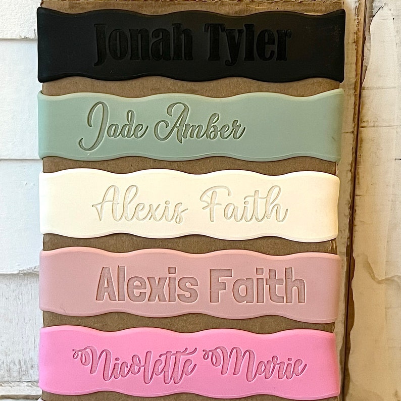 May include: Five personalized name tags with wavy edges. The tags are in black, green, white, pink, and light pink. The names on the tags are Jonah Tyler, Jade Amber, Alexis Faith, Alexis Faith, and Nicolette Marie.