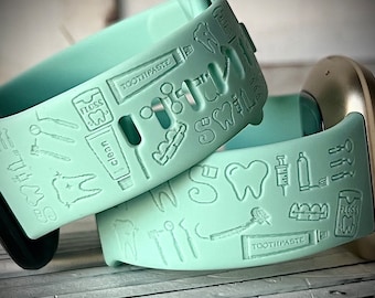 May include: Two mint green silicone watch bands with a dental theme. The bands are covered with small white embossed images of teeth, toothbrushes, floss, toothpaste, and other dental tools. The text "TOOTHPASTE" and "FLOSS" are visible on the bands.