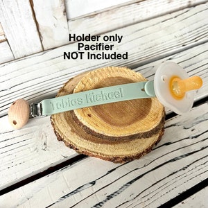 Pu&ograve; includere: Un portaciuccio in silicone verde chiaro con un perno di legno e un fermaglio. Il portaciuccio &egrave; personalizzato con il nome "Tobias Michael". Il ciuccio non &egrave; incluso.