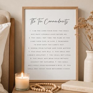 May include: A framed wall art print featuring the text The Ten Commandments in a black serif font on a white background. The list includes ten numbered religious directives. The print is displayed in a light wood frame with a clean, simple design.