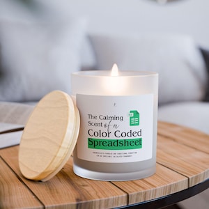 Peut inclure: Une bougie en verre dépoli allumée avec un couvercle en bois est posée sur une table en bois. L'étiquette de la bougie indique "The Calming Scent of a Color Coded Spreadsheet". C'est un article de décoration.