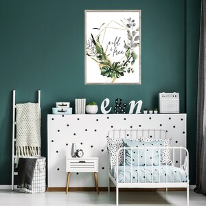 May include: A white framed print with a gold geometric design and green foliage. The print says "wild & free" in black lettering.