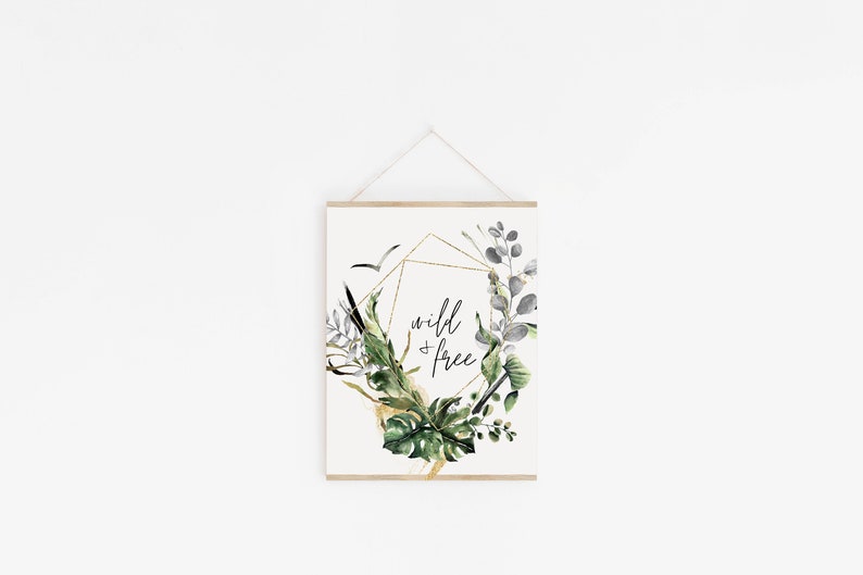 May include: A white poster with a gold geometric frame and green and grey watercolour leaves. The text "wild & free" is written in black inside the frame.