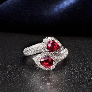 Op de afbeelding: Een zilveren ring met twee peervormige rode robijnen gezet in een halo van diamanten. De ring is ontworpen met een gedraaide band.