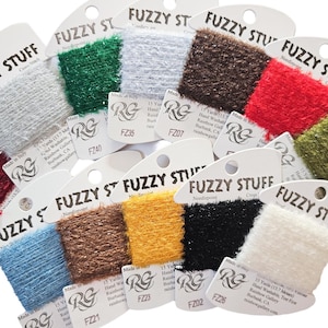 May include: A collection of spools of Fuzzy Stuff yarn in various colors, including white, green, brown, red, and blue. Each spool is labeled with the text "FUZZY STUFF" and product information.