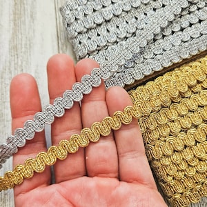 May include: Two spools of decorative trim, one gold and one silver. The trim is a braided, rope-like design with a scalloped edge.