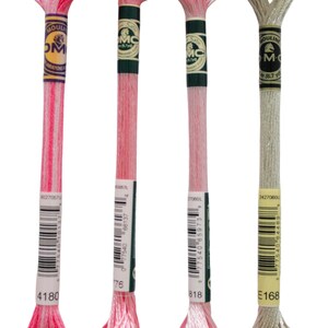 May include: Four spools of DMC embroidery floss. The spools are labeled with the DMC numbers 4180, 176, 818, and E168. The floss colors are pink, pink, pink, and light gray.