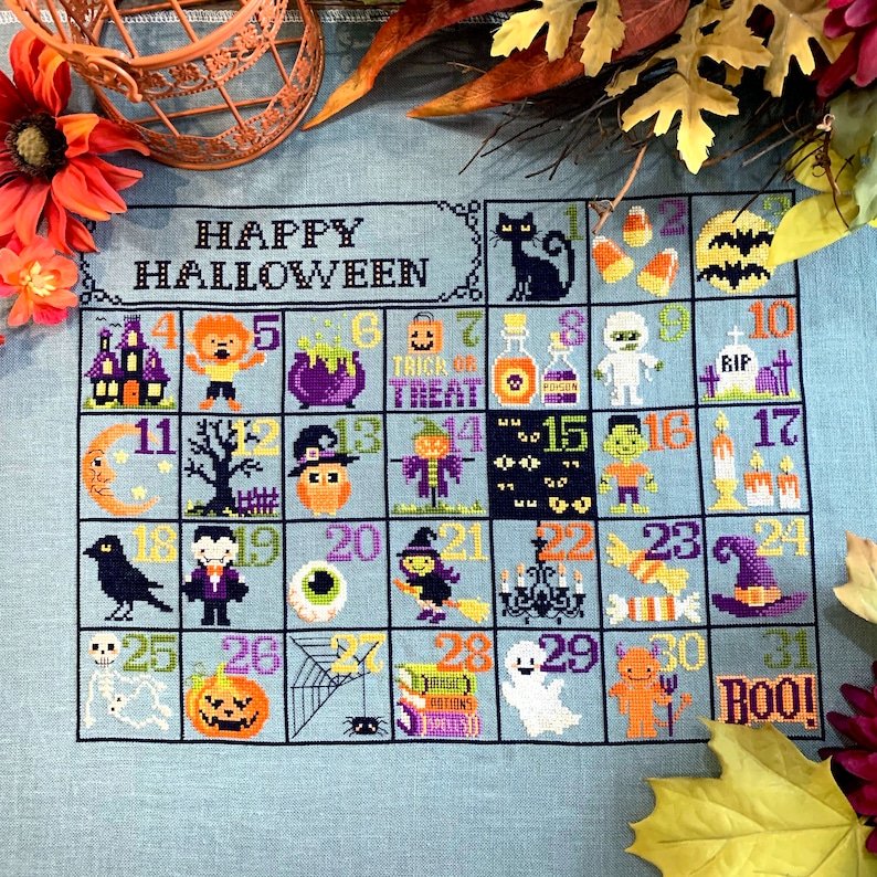 Peut inclure: Un motif de point de croix d'un calendrier d'Halloween avec une vari&eacute;t&eacute; d'images effrayantes et mignonnes, y compris un chat noir, un fant&ocirc;me, une citrouille, une sorci&egrave;re et un vampire. Le calendrier est sur un fond bleu avec les mots "Happy Halloween" en haut.