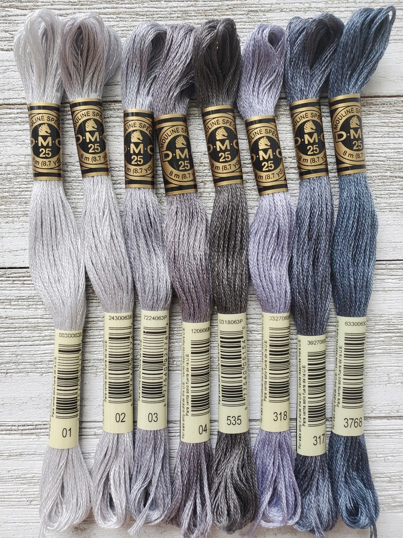 May include: Eight spools of DMC embroidery floss in shades of gray, from light to dark. Each spool has a white label with the DMC logo, the number, and the text "Mouline Special" and "DMC 25".
