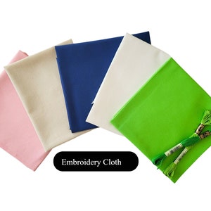 May include: A selection of coloured embroidery cloth squares in pink, beige, navy blue, white, and green. Two bundles of green embroidery floss are also included. The text "Embroidery Cloth" is displayed in a black rectangle.