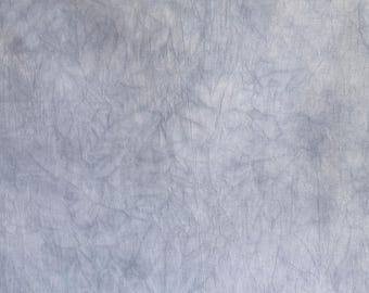 May include: A close-up of a piece of fabric with a textured, wrinkled appearance. The fabric is a light blue-gray color, with darker areas creating a mottled effect. The material appears to be linen or a similar woven textile.