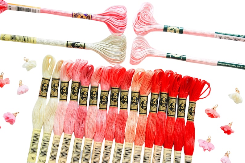 May include: A collection of 25 embroidery floss spools in shades of pink, red, and cream. The spools are arranged in a gradient from light to dark. Each spool has a gold label with the text "DMC 25" printed on it.
