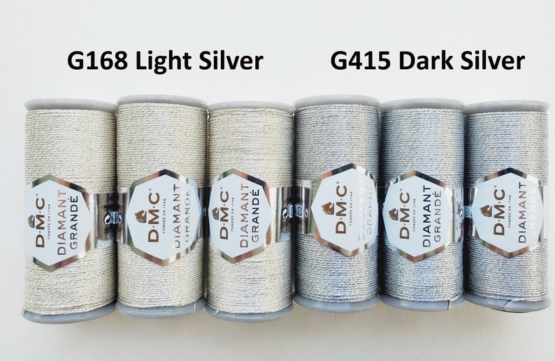 May include: Six spools of D.M.C. Diamant Grande thread in light and dark silver. The labels read "G168 Light Silver" and "G415 Dark Silver". The thread is wound on gray spools with silver labels.