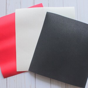 May include: Three fabric swatches, one red, one white, and one black. The swatches are laid out on a white wooden surface.